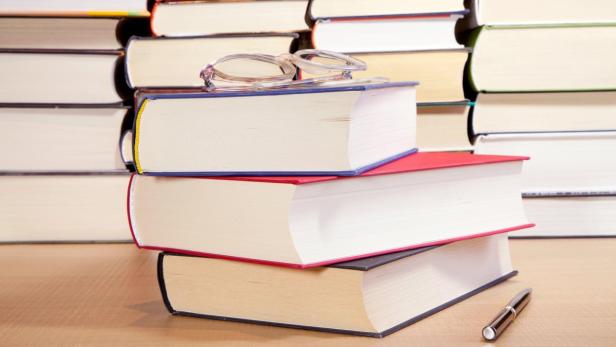 Ein Stapel aus drei Büchern mit Brille und Stift auf einem Tisch.