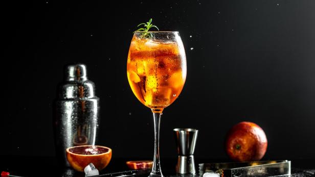 Ein Aperol Spritz wird mit einer Orangenscheibe und Rosmarin garniert.