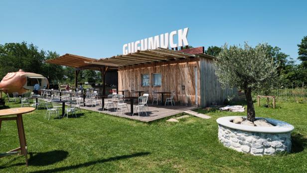 Das Restaurant „Gugumuck“ mit Tischen und Stühlen im Freien an einem sonnigen Tag.