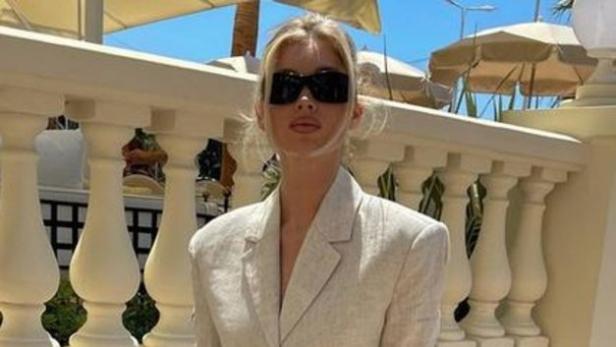 Eine blonde Frau trägt einen beigen Blazer und Shorts mit schwarzen Loafers.