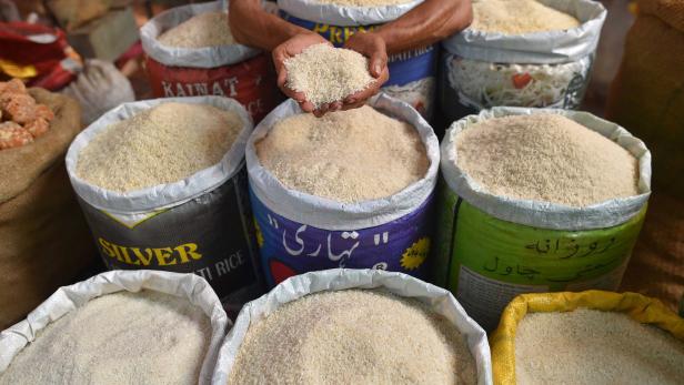 Ein Mann hält eine Handvoll Reis vor mehreren Säcken Reis auf einem Markt.