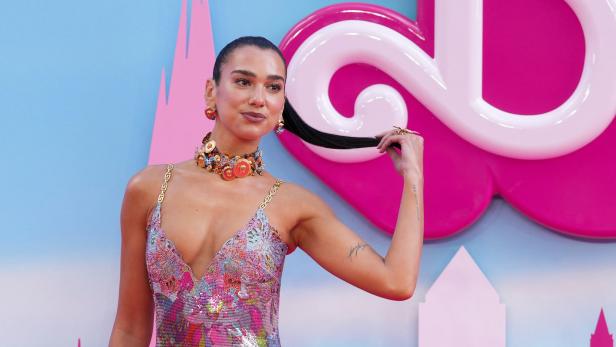 Dua Lipa posiert in einem bunten Kleid auf einem pinkfarbenen Teppich.