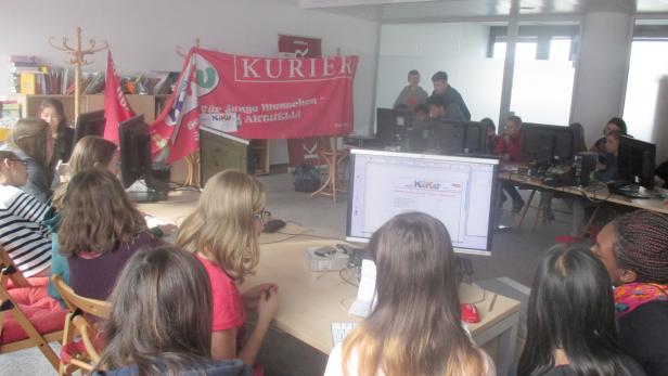 Eine Gruppe von Schülern arbeitet an Computern in einem Klassenzimmer mit einem „Kurier“-Banner.