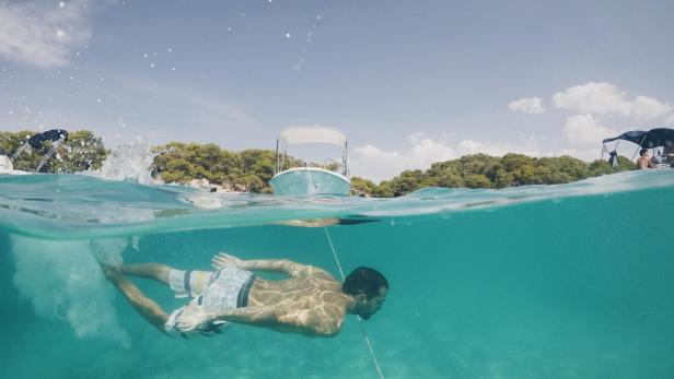 Ein Mann schwimmt im türkisfarbenen Wasser vor Menorca.