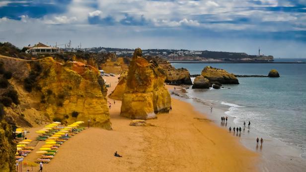 Blick auf den Strand Praia do Camilo in Lagos, Portugal, mit gelben Felsformationen und Menschen.