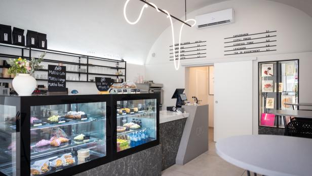 Innenansicht eines modernen Cafés mit Theke, Kuchenvitrine und Menütafel.