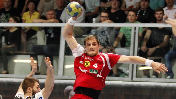 Ein Handballspieler in rotem Trikot wirft den Ball.