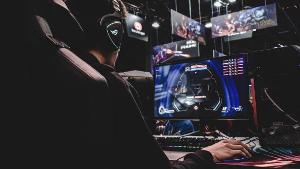 Ein junger Mann spielt ein Computerspiel mit Headset und blickt auf den Monitor.