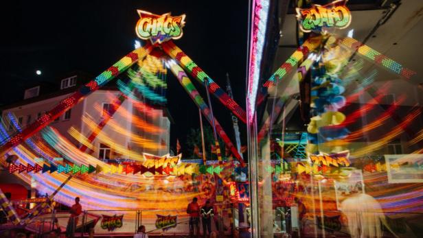 Ein bunt beleuchtetes Fahrgeschäft namens „Chaos“ dreht sich auf einem Jahrmarkt bei Nacht.