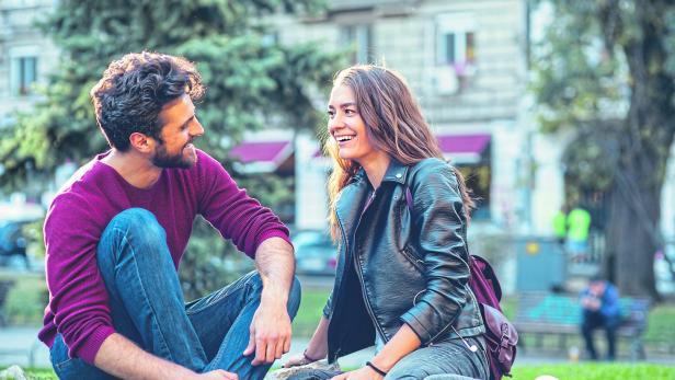 Ein junges Paar sitzt lachend im Park.