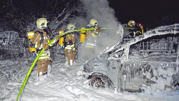Feuerwehrleute löschen ein brennendes Auto mit Schaum.