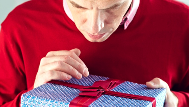 Ein Mann in rotem Pullover betrachtet ein blau verpacktes Geschenk mit roter Schleife.