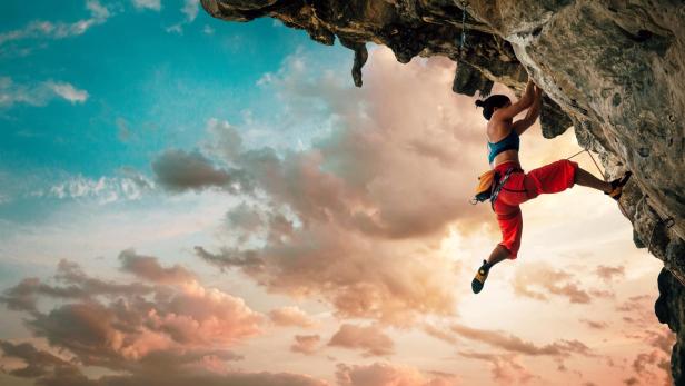 Eine Frau klettert an einer Felswand vor einem dramatischen Himmel.