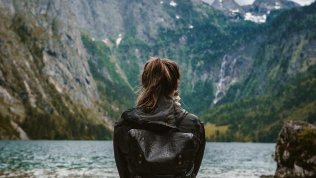 Eine Frau mit Rucksack sitzt am Ufer eines Bergsees.