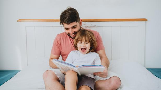 Father reading fun book to son in bed