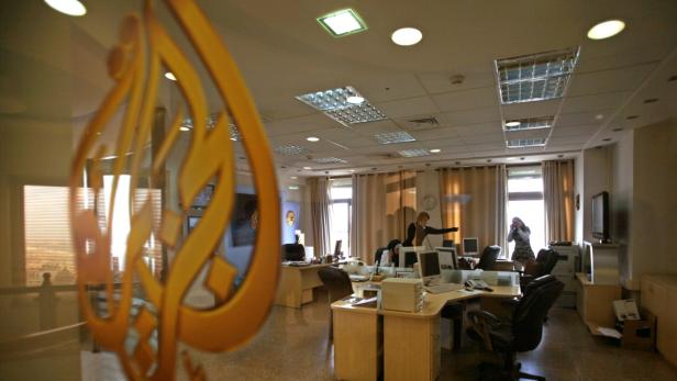 Büro von Al Jazeera mit Mitarbeitern bei der Arbeit hinter einem Logo an der Tür.
