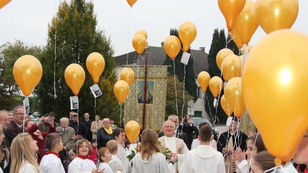 Eine Prozession mit einem Priester, Ministranten und goldenen Luftballons.