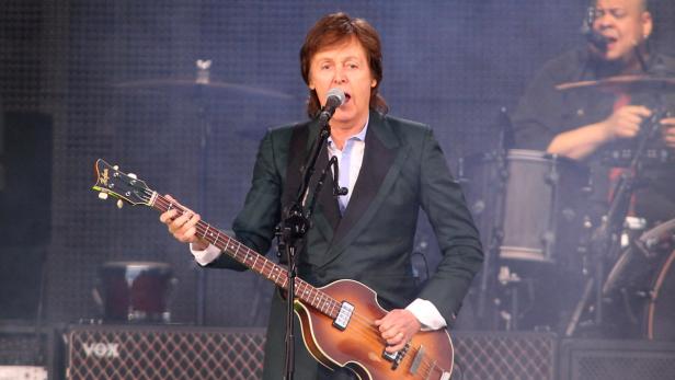 Paul McCartney spielt Bassgitarre und singt auf der Bühne.