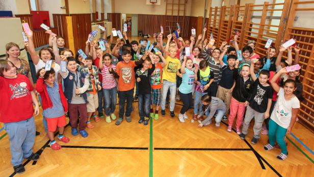 Eine Gruppe Schulkinder steht in einer Turnhalle und hält selbstgebastelte Gegenstände hoch.