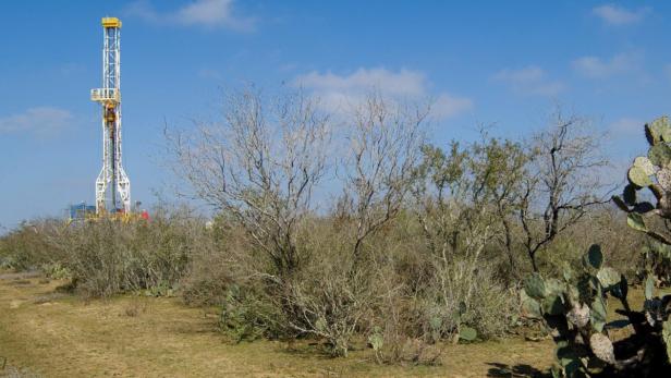 Ein Bohrturm steht inmitten von Büschen und Kakteen unter blauem Himmel.