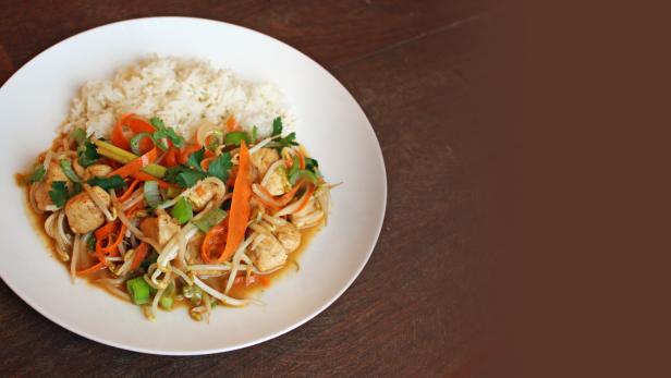 Ein Teller mit Hühnchen-Gemüse-Pfanne und Reis.