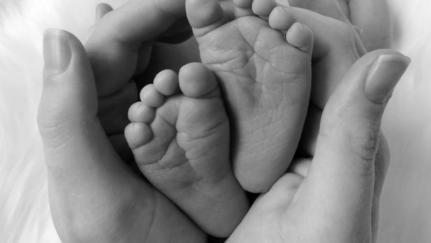 Eine Berlinerin sorgt mit ihrem Babyglück für Schlagzeilen: Alexandra Hildebrandt hat mit über 60 ihr zehntes Kind zur Welt gebracht. Schwarz-weiß Nahaufnahme von Händen, die kleine Babyfüße halten