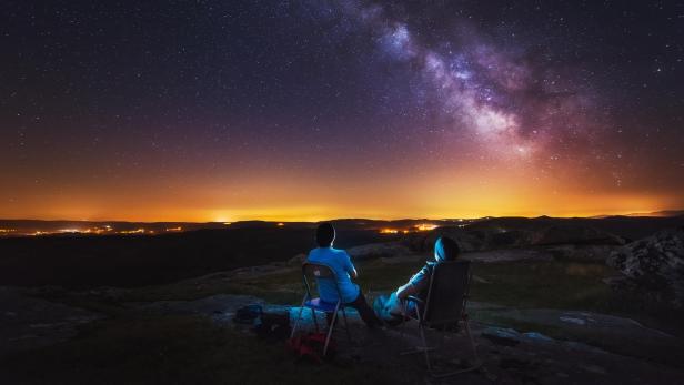 Zwei Personen sitzen unter der Milchstraße und schauen in den Nachthimmel.