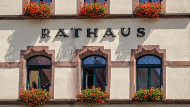Die Fassade eines Rathauses mit roten Blumen vor den Fenstern.