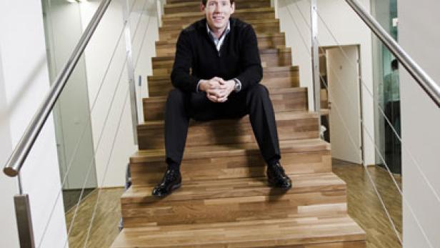 Ein Mann sitzt auf einer Holztreppe in einem modernen Gebäude.