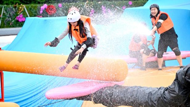 Eine junge Frau balanciert auf einem Hindernisparcours und wird mit Wasser bespritzt.
