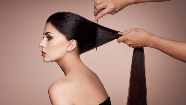 Ein Friseur kämmt das lange, dunkle Haar einer Frau.