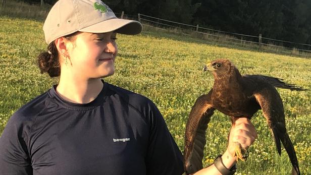 Links eine junge Frau mit beiger Kappe und einem schwarzen t-shirt, daneben eine braune Rohrweile, ein kleiner Greifvogel