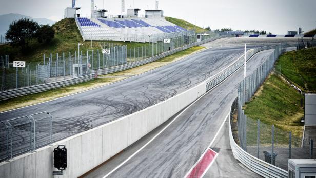 Eine leere Rennstrecke mit Reifenspuren und Tribünen im Hintergrund.
