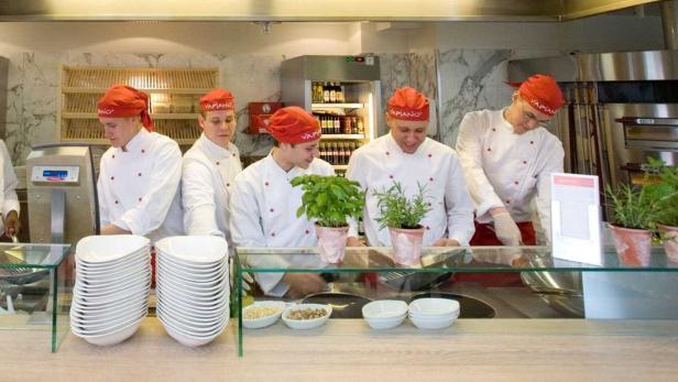 Mehrere Köche in roten Mützen arbeiten in einem Vapiano-Restaurant.