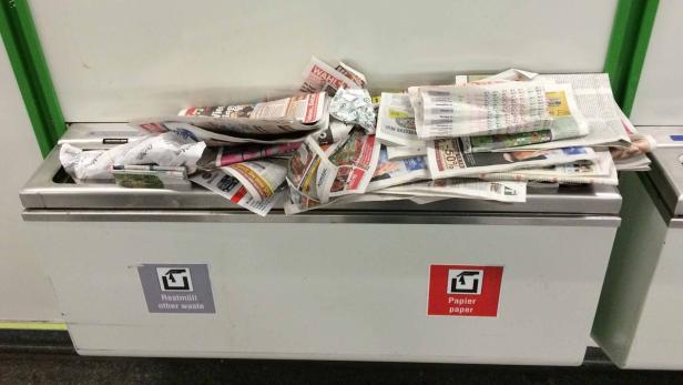 Ein überfüllter Papierkorb mit Zeitungen und anderem Papiermüll.