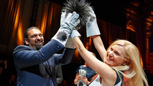 Zwei Personen mit Handschuhen halten eine stachelige Kugel hoch und lächeln.