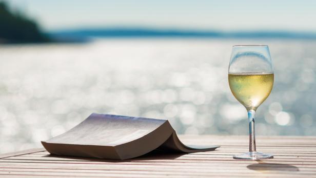 Ein Glas Wein und ein Buch auf einem Holztisch mit Blick auf das Meer.