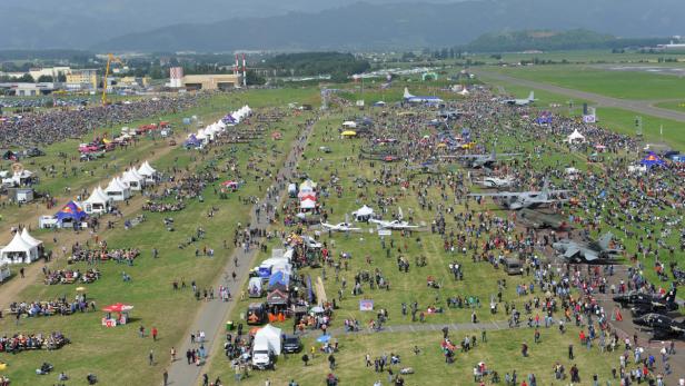Eine große Menschenmenge besucht eine Flugschau mit zahlreichen Flugzeugen und Zelten.