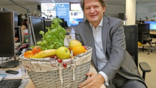 Ein Mann in einem Büro sitzt neben einem Korb mit Obst und Gemüse.