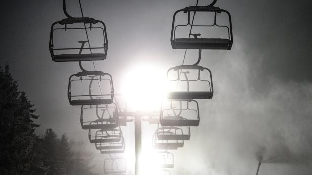 Eine Gondelbahn hängt im Nebel über einer Skipiste.