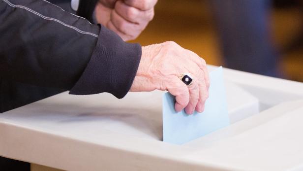 Eine Hand wirft einen blauen Wahlzettel in eine Wahlurne.