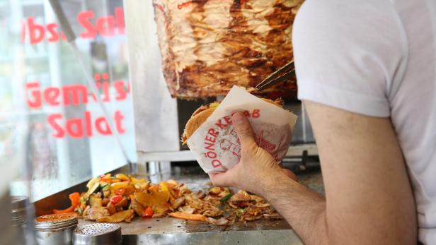 Mann steht vor Dönerspieß und bereitet ein Kebab-Sandwich zu