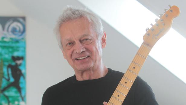 Ein lächelnder Mann mittleren Alters hält eine E-Gitarre der Marke Fender.