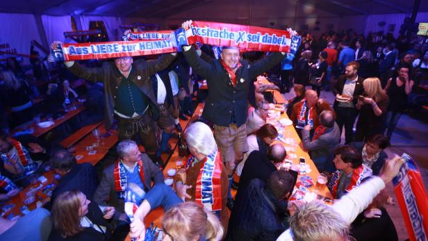 Menschen in Tracht feiern in einem Festzelt mit Schals mit der Aufschrift „Aus Liebe zur Heimat“.