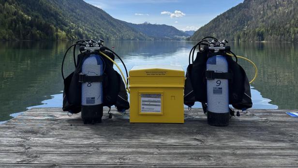 Gelber Briefkasten zwischen zwei Sauerstoffflaschen auf einem Steg, dahinter ein See
