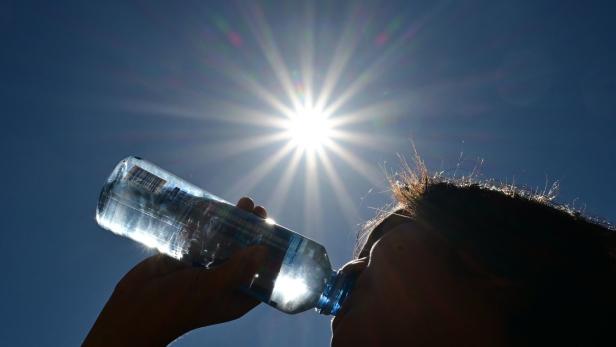 Mann trinkt aus Wasserflasche in der prallen Sonne.