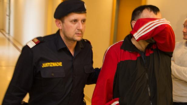 Ein Justizbeamter führt eine Person ab, die ihr Gesicht verdeckt.