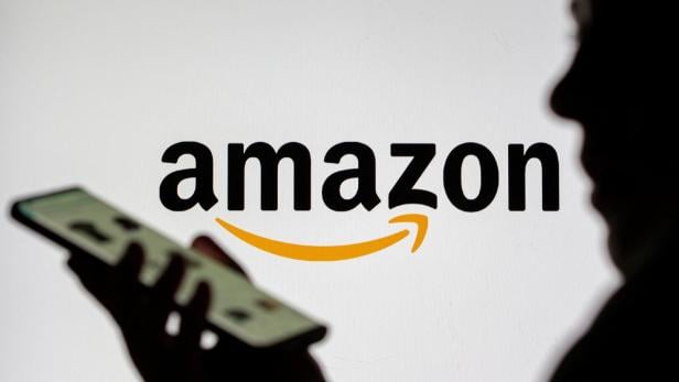 Amazon sucht Influencer*innen, zahlt aber nur wenig. Eine Person hält ein Smartphone vor dem Amazon-Logo mit dem charakteristischen gelben Pfeil.