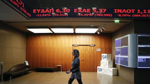 Eine Frau geht in einer Börse unter einer Anzeigetafel mit griechischen Aktienkursen entlang.