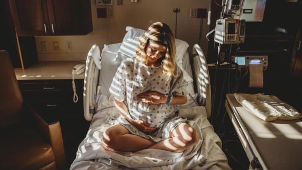 Pregnant woman touching stomach while sitting on bed in hospital - Stock-Fotografie